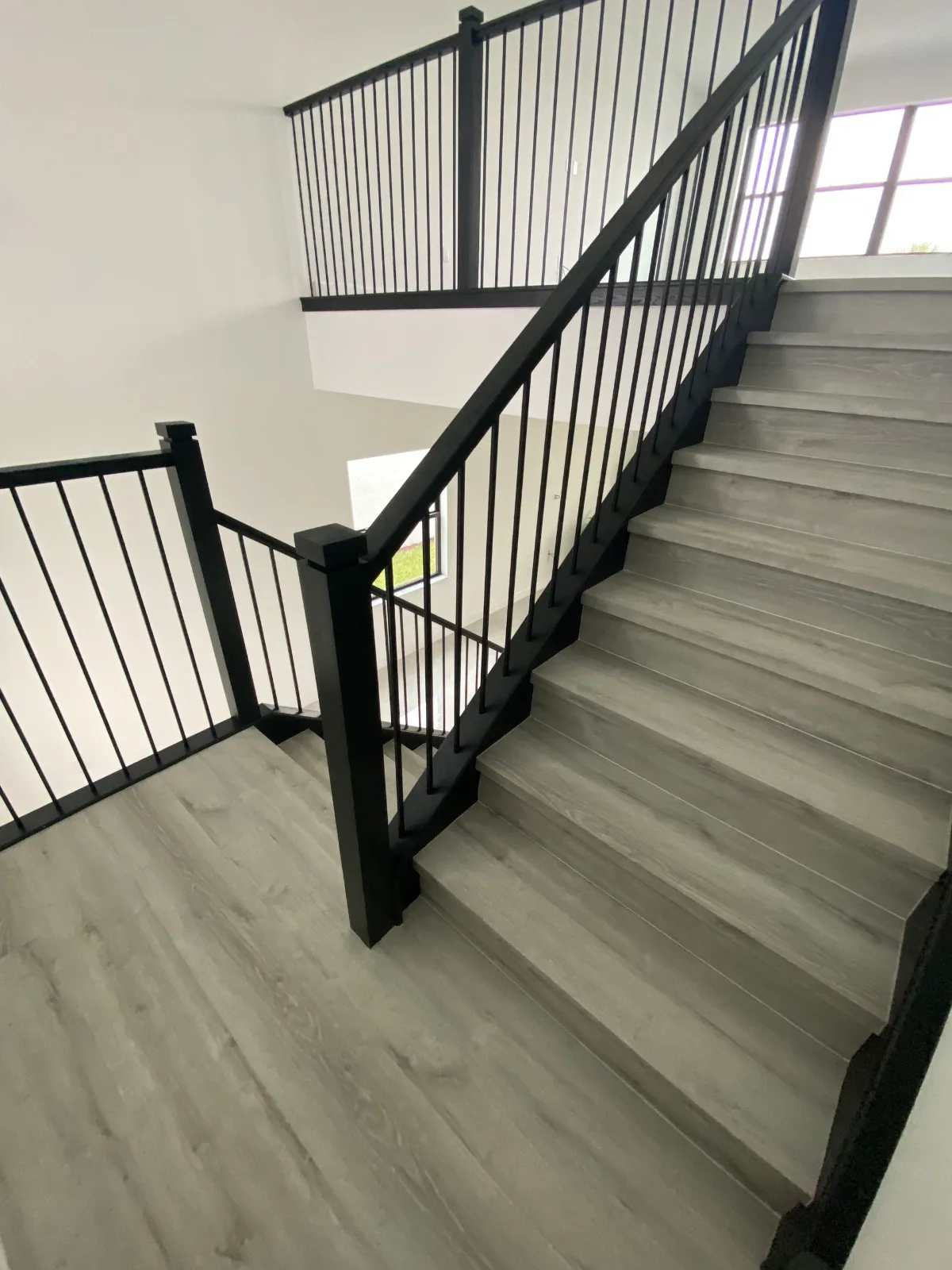 Grey SPC vinyl stair treads with white vinyl risers and black iron balusters installed in a Southwest Florida home